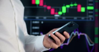 Ciddi iş adamı iş yerinde cep telefonundan mesaj yazıyor. Hırslı tüccar, plazma ekranında renkli diyagrama karşı parlak bir banka kartı gösterdi