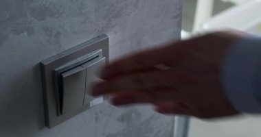 İnsan eli, duvardaki gümüş ışık düğmesine mavi duvar kağıdıyla basar ve lambayı açar. El, ışık düğmesine basar ve ışığı kapatır.