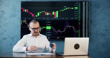 Gözlüklü bir tüccar belgeleri kontrol eder ve bilgisayar ekranına bakar. Ciddi işadamlarından ofiste plazma ekranının başında oturan ortağa çağrı