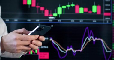İş kıyafetlerindeki nüfuz edici plazma ekranında dinamik oran tablosuna karşı telefon tutuyor. İş adamı, işyerindeki çalışma saatleri hakkında mesaj yazar.