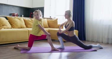 Sarışın bayan kızına evde esneme egzersizi yapmayı öğretiyor. Anne ve kız evde pilates çalışmasından önce birlikte esniyorlar.