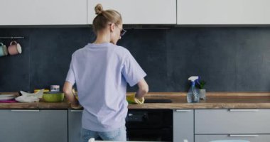 Sarışın kadın mutfakta elektrikli sobayı temizledikten sonra bez atıyor. Geniş mutfağı temizledikten sonra ev hanımı yorgun görünüyor.