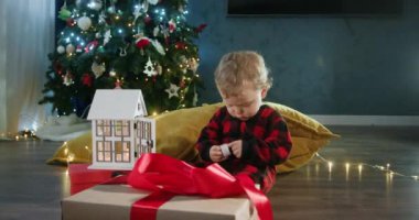 Rahat pijamalı çocuk Noel hediyesini karton kutunun içinde açıyor. Heyecanlı suratlı çocuk oyuncak evine mum koyuyor.