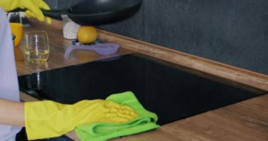 Ev hanımı mutfaktaki kirli parçacıklardan elektrikli sobayı temizliyor. Lastik eldivenli kadın mutfaktaki kirli fırından tavayı çıkarıyor.