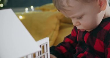 Konsantre olmuş, rahat pijamalı çocuk Noel 'de alınan beyaz bebek evini incelemekten zevk alıyor. Çocuk evdeki oyuncak evine mum koyuyor.