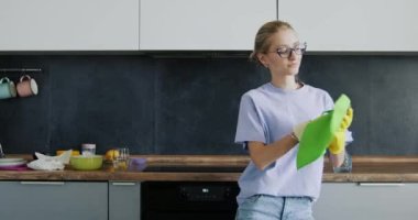 Bardaklı genç bir kadın mutfakta dans ediyor. Geniş bir dairede bulaşıkları yıkıyor. Rahat giyimli ev hanımı evde ev işi yapmaktan hoşlanıyor.