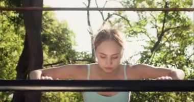 Mutlu genç kadın dışarıda spor giyim kuşamında parlak güneş ışığında antrenman yapıyor. Bayan sporcu, şehir bahçesinde uzun süren beden eğitimi eğitiminden önce ısınıyor.