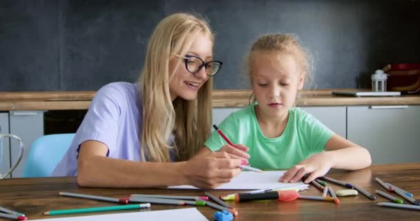 ブロンドの教師は 色鉛筆を使用して絵を作る方法を少女の生徒を示しています 女性教師と女子高生が座って自宅のアートレッスンで机に描画 — ストック動画