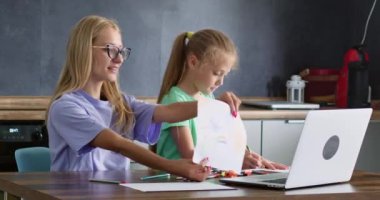 Anne ve kızı online sanat dersine katılıyorlar. Mutlu kadın, uzaktan ders sırasında çizilen fotoğrafları dizüstü bilgisayara gösteriyor. Evde eğitim ve aile