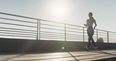 Genç bayan koşucu silueti, telefonları kontrol etmek ve rahatlamak için eğitimini durdurdu. Spor kıyafetli bir bayan sporcu kaldırımda koşar ve telefon ekranına bakar.