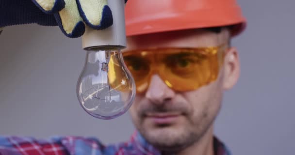 工人们戴着安全眼镜和安全帽螺丝在灯泡里 技师勤奋地检查建筑物内的实际电力状况 — 图库视频影像