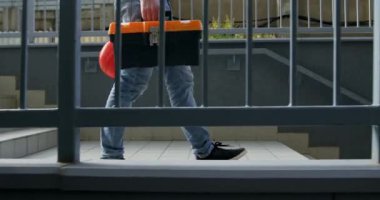 İnşaat aletleri kutusuyla aşağıda yürüyen inşaatçı bacakları. İşçiler merdivenlerden inerken araç gereç taşıyorlar.