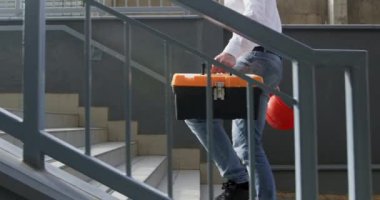 İnşaatçı, alet çantası taşıyan merdivenlerden inerek inşaat ustalığı gününe koruyucu miğfer de getirmiş. Günlük görevleri yerine getirmek için profesyonel yol