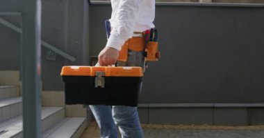 Adam işe giderken merdivenlerden yukarı çıkıyor. Alet çantası ve güvenilir alet kemeriyle yüklenmiş işçiler işe dalmaya hazır bir şekilde merdivenlerden yukarı çıkıyorlar.