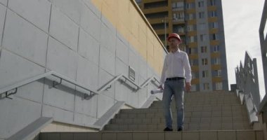Miğferli özenli mimar binanın merdivenlerinden inen inşaat planını dikkatlice gözden geçiriyor. Çizim planı konseptine uyma konusunda uzman denetimi