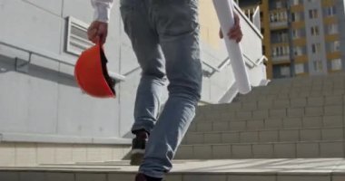 Profesyonel mimar kask ve taslak rulo ile merdivenlerden çıkar. Mühendis, iş yerine giderken çizim merdiveni taşıyor.