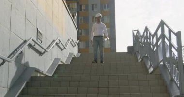 Mimar, inşaat planlarını dikkatlice gözden geçirmek için merdivenlerden iniyor. Uzman, projenin her adımında hassasiyeti ve titizliği gözlemliyor