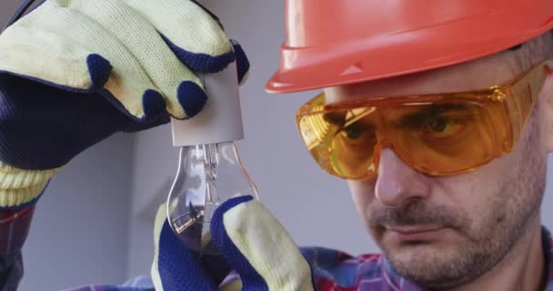Elektricien Helm Met Beschermende Bril Controleert Nauwkeurig Gloeilamp Man Wordt — Stockvideo