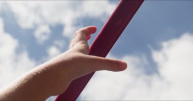 Sportif çocuk eli, yazın bulutlu gökyüzüne karşı yatay çubuğu sıkıca kavrıyor. Aktif çocuk sıcak bir günde kollarını esnetiyor.