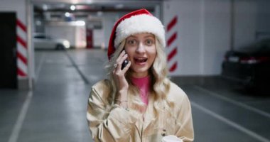 Noel Baba şapkalı sarışın kadın yeraltı otoparkında telefonla konuşuyor. Kadın, öpüşürken yüz ifadesiyle selfie çekiyor.