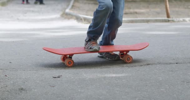 信頼できる少年が夏の日に都市公園で乗る準備をするスケートボードに足を踏み入れる 太陽の訪問者のプリスクーラーは新鮮な空気で週末を過ごします — ストック動画