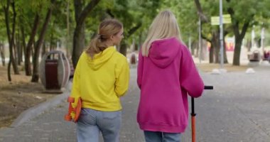 Kızların en iyi arkadaşları parktan kaykay ve scooterla geçer. Pembe ve sarı kapüşonlu mutlu genç kızlar şehir sokaklarında kahve içerler.