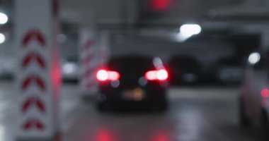 Araba, iş yerindeki geniş otoparktan sorunsuzca çıkıyor. Arka farlar loş bir çevreye yumuşak bir ışık saçıyor.