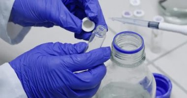 Teknisyenler laboratuvar kapanışında cam şişeye pipetle su damlatırlar. Modern tıp merkezinde akışkan madde örnekleri inceleniyor