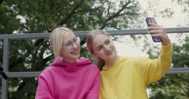 Bayan en iyi arkadaşlar parkta akıllı telefon kullanarak selfie çekerler. Memnun kızlar parktaki bayramları hatırlamak için fotoğraf çekerler. Gerçek arkadaşlık.