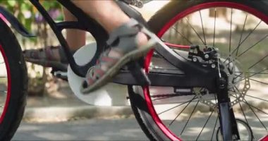 Oğlan, yaz parkında bisiklet sürmeyi öğrenme mücadelesi veriyor. Çocuk pedallar geri gidiyor. Bacak hareketlerinin nüanslarını öğreniyor.