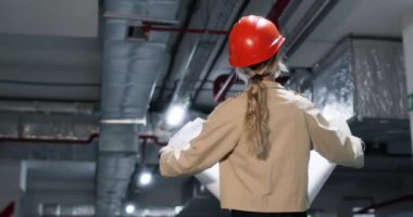 Miğferli kadın, yeraltında yürürken çizim yapıyor. Sarışın kadın mühendis binanın yapısal bileşenlerini inceliyor.