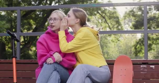 身材瘦小的姑娘们坐在长椅上闲聊着 她们还拿着滑板车和滑板 快乐的青少年在溜冰场消磨时光之前 先讨论新发现的消息 — 图库视频影像