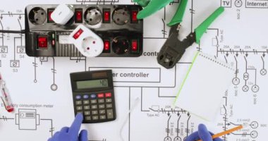 Elektrikçiler ağ yükleme cihazlarını prizin üst görüntüsüne kadar test ediyorlar. Mühendisler çizimler üzerinde merkezi denetleyici güvenlik sistemi üzerinde çalışıyorlar