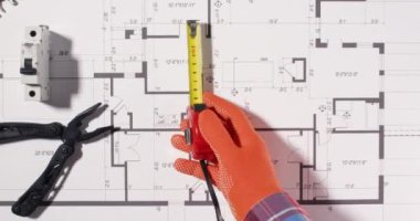 Teknisyen, evin üst manzarasına uygun bir yer bulmak için çevreyi tedbir alıyor. Mühendis planlara elektrik uyarı etiketleri ekliyor.