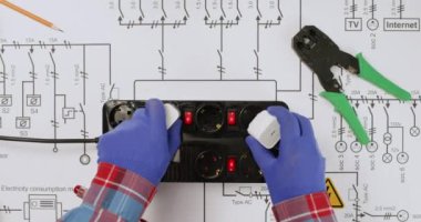 Elektrik prizine bağlı bir elektrikçi yukarıdan elektrik şematik diyagramı görüntüsünü aktarıyor. Ağ planında yükleme aygıtları