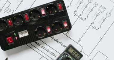 Elektrikçi voltajı çokölçer ile kontrol eder ve üst görüş üzerine uyarı işareti uzatma prizleri koyar. İşçi elektrik ağının güvenliğini kontrol ediyor