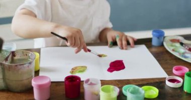 Küçük sanatçı farklı efektler görmek için çeşitli renkler deniyor. Küçük çocuk evde resim dersi sırasında yaratıcı fikirleri dönüştürüyor.