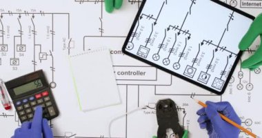 Elektrikçiler kağıt planındaki elektrik devresi şebekesinin voltajını sayıyorlar. Uzmanlar şematik diyagramda tablet ve hesap makinesi kullanırlar