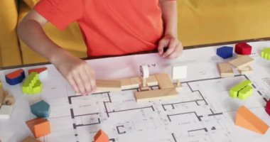 Küçük çocuk, mimari planlar üzerine ahşap bloklardan yollar inşa ediyor. Yaratıcı çocuk evde inşaat setiyle oynuyor. Yürüyen çocuk oyuncakları