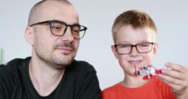 Neşeli oğul ve baba evde ağır çekimde uçak oyuncağıyla oynuyorlar. Mutlu ebeveyn ve küçük çocuk oyun odasında kendi kendine kurulmuş uçakla gurur duyuyor.