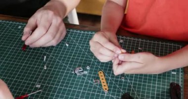 Küçük çocuk, babasıyla yakın çekimde inşaatçının küçük detaylarını birbirine bağlıyor. Anne ve babası, bebeğe evde metal parçaları monte etmede yardımcı oluyor.