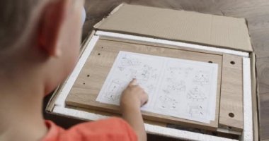 Baba, çocukça şeyleri açıklayan bir resim çiziyor. Anaokulu çocuğu mobilya montajı talimatlarına bakıyor.