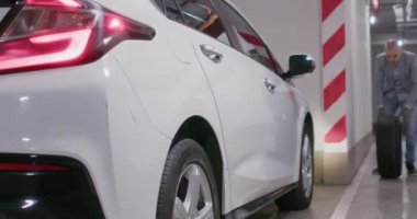 Sürücü lastik değiştirmek için lastiği arabaya yuvarlıyor. Adam yeraltı garajında kullanılması kolay olsun diye aracın yanına tekerlek bırakıyor.