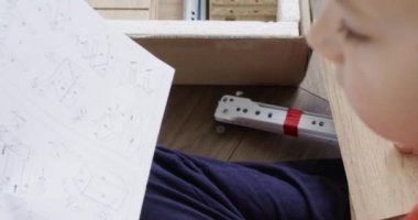 Genç çocuk mobilyaları bir araya getirirken montaj talimatlarını dikkatle okuyor. Göreve odaklandı, diy projesine el attı, öğrenme ve beceri geliştirme sergiliyor.