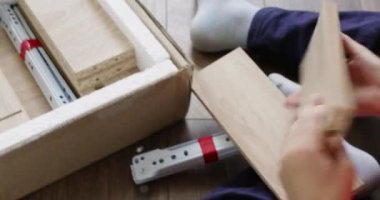 Anaokulu öğrencisi, eşyaların montajı için paketlenmemiş kutulardan çıkar. Genç çocuk ahşap levhaları toplayarak talimatları dikkatle izler.