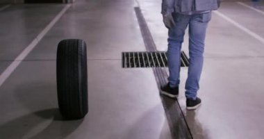 Sürücü yeraltı garajında tekerlek yuvarlamaya paralel yürüyor. Adam sakince eski yazlık lastiği depolamak için doğru yere koymak için daireye doğru gidiyor.