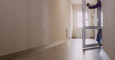 Su şişeli kurye koridora girerken kapıyı açıyor. Eldivenli teslimatçı müşteriye büyük bir plastik sıvı kabı taşıyor.