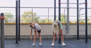 Kadın ve kız şehir spor sahasında ileri doğru eğiliyor. Kızı anneyi izliyor ve gövdesiyle sırt egzersizi yaparak özel hareketleri taklit ediyor.