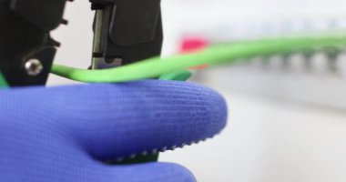 Elektrikçi adam eldivenleri elektrik şalterinden yeşil kabloyu kesmek için kerpeten kullanıyor. Eldiven ustası tamirat işiyle uğraşıyor.