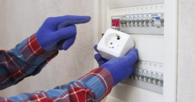 Elinde elektrik prizi olan adam sigorta kutusunu kapatıyor. Lastik eldivenli elektrikçi evdeki elektrik sistemini açıklıyor